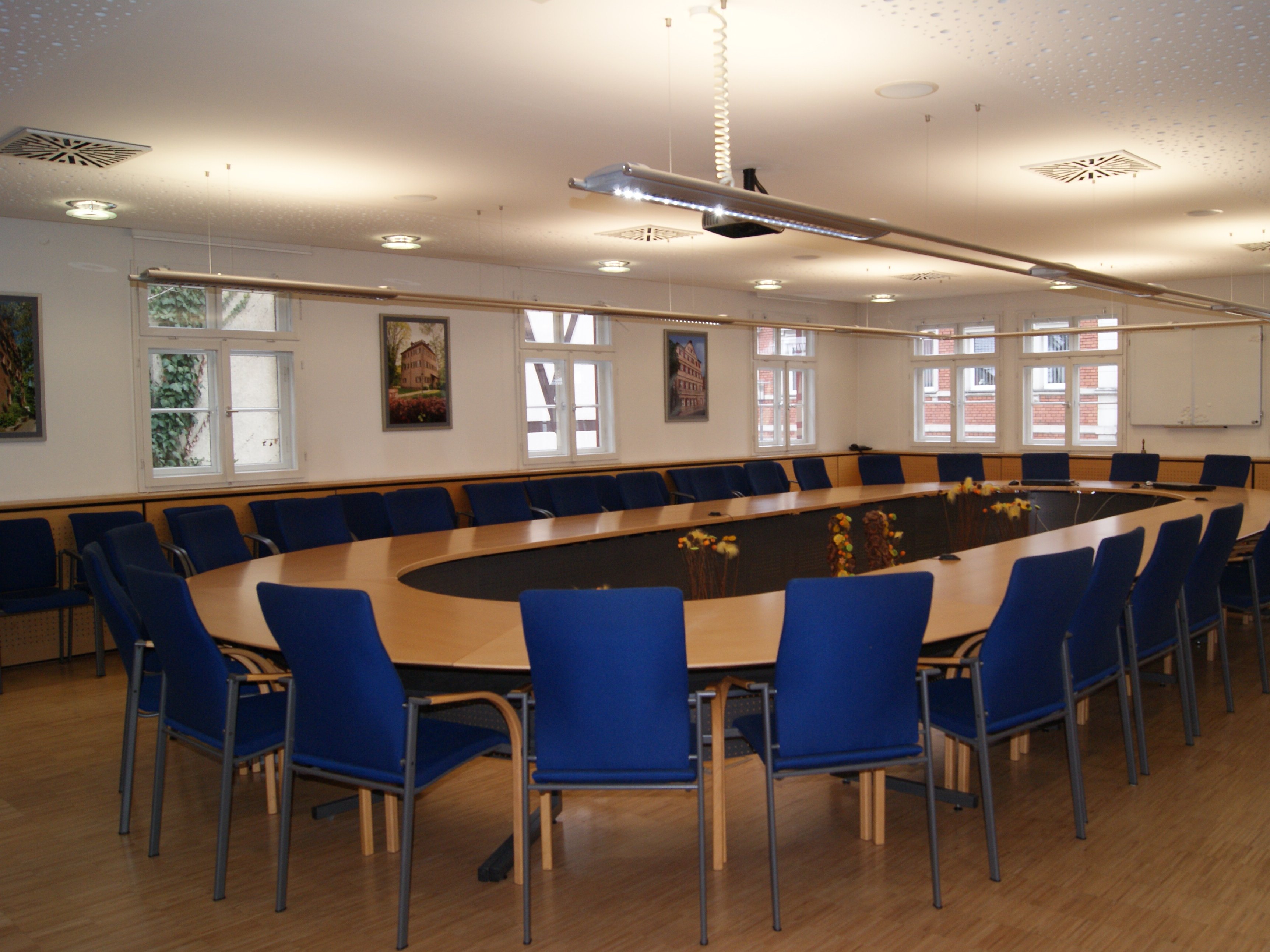 Sitzungssaal im Rathaus mit ovalem Tisch und Bildmotiven von den Schlössern