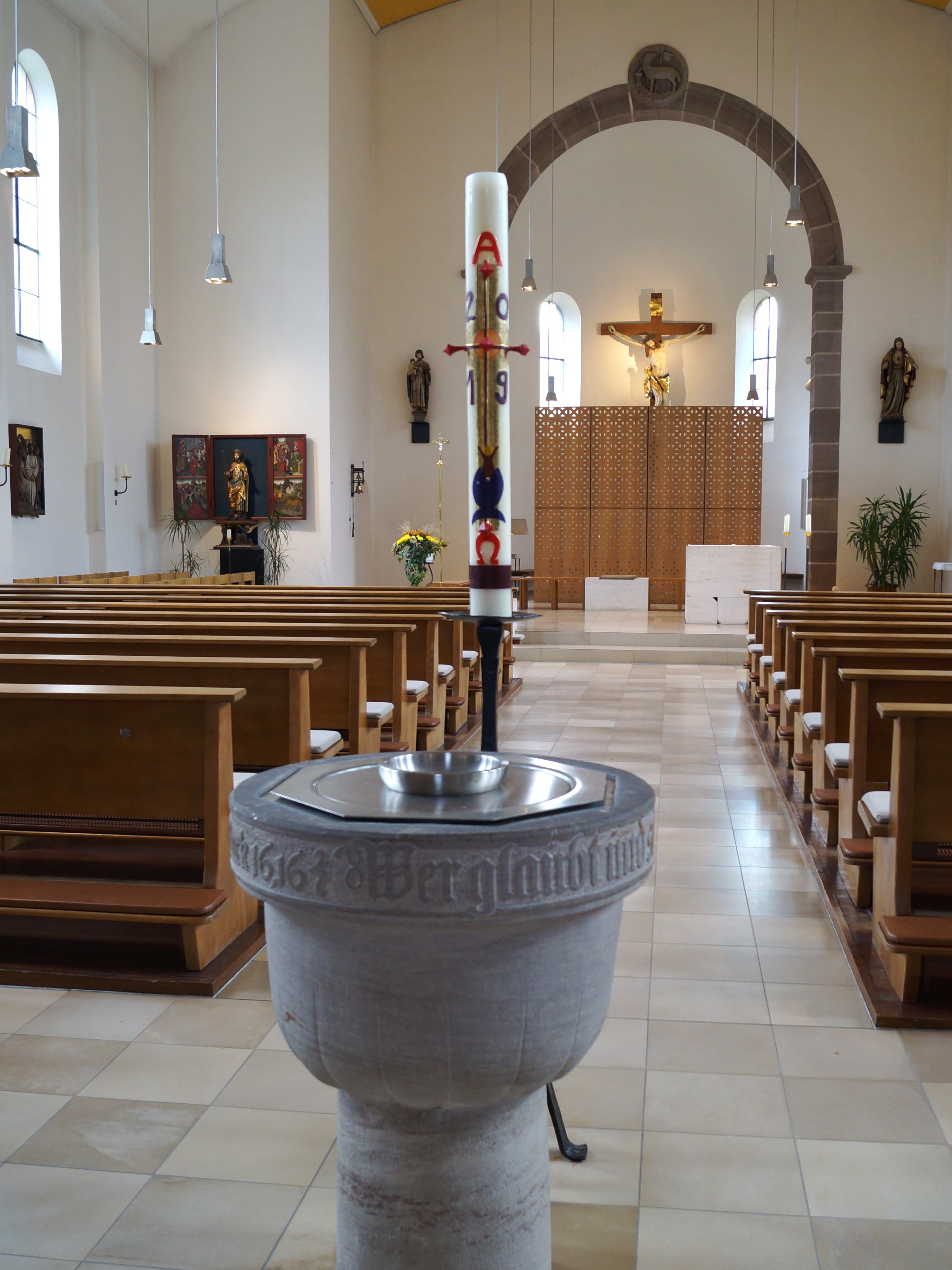 Das runde Taufbecken der katholischen Kirche mit dem Altar im Hintergrund