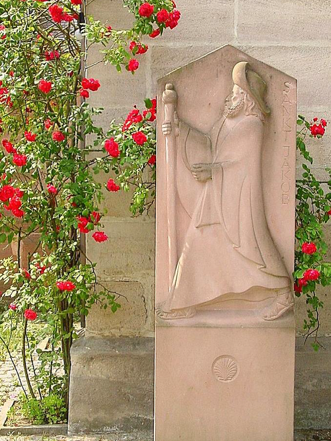 Der schreitenden Jakobus, gehauen aus rotem Sandstein, umgeben von roten Rosen