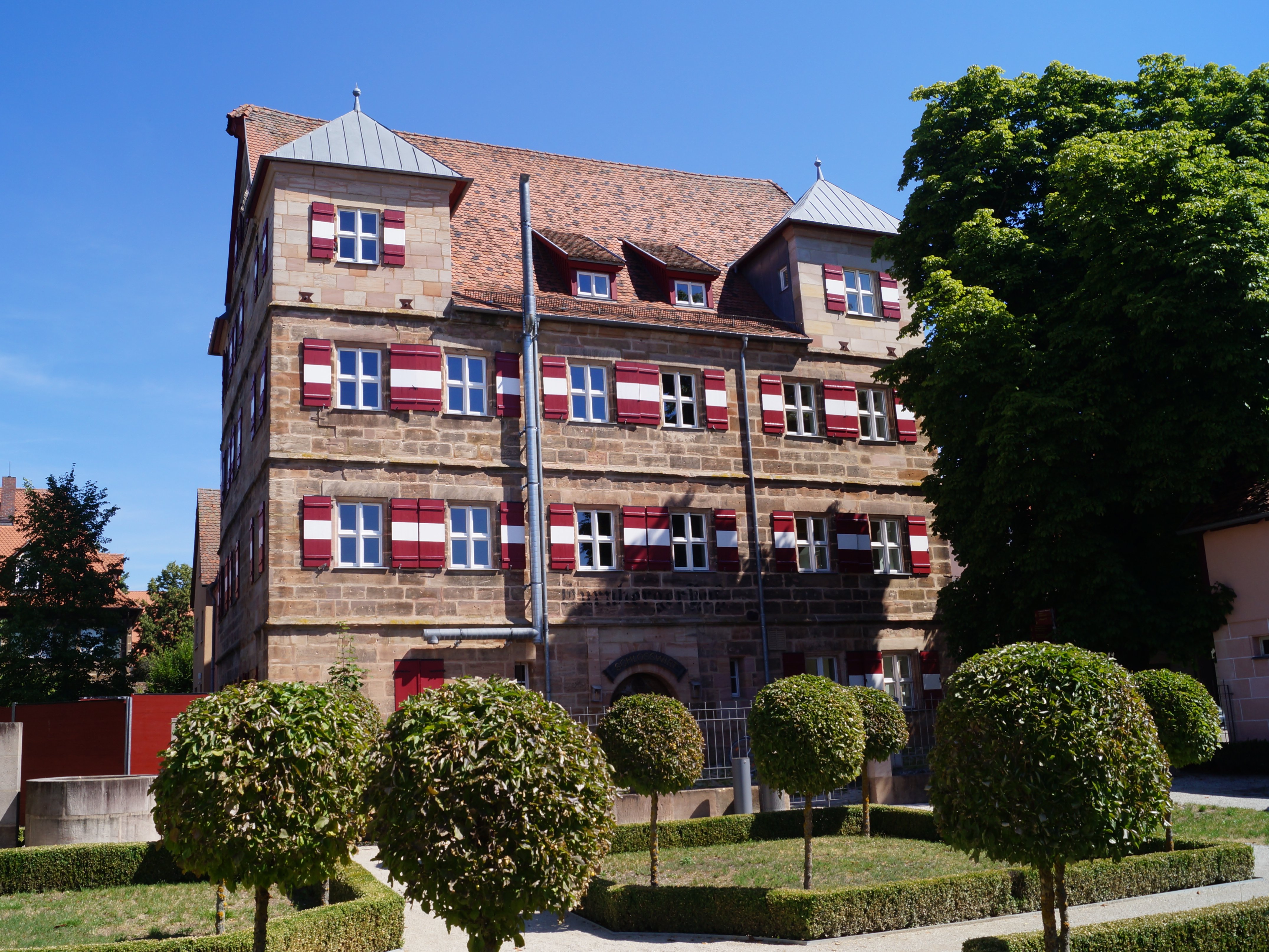 Vue du jardin baroque sur le château de Tucher aux volets rouges et blancs
